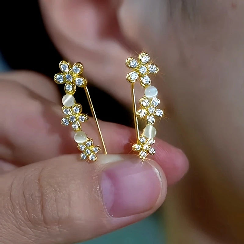 Pair of gold flower cat's eye crystal ear climber earrings held between fingers