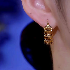 Gold hollow crystal huggie hoop earring worn on ear, side close-up view