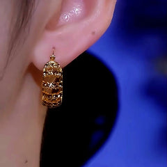 Gold hollow crystal huggie hoop earring worn on ear, front close-up view