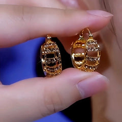 Pair of gold hollow crystal huggie hoop earrings held between fingers, close-up