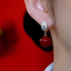 Model showcasing the dangle and style of the 14K Gold-Plated Diamond Leaf Red Bead Earrings