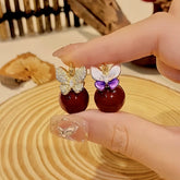 Pair of mismatched butterfly red bead drop earrings held in hand