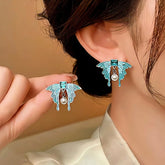 Women's turquoise butterfly pearl dangle earrings, hand holding matching pair