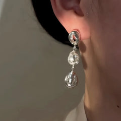 Model showcasing the dangle and style of the 14K Gold-Plated Elegant Hollow Three-Layer Water Drop Earrings