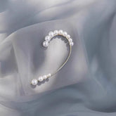 Gold-toned graduated pearl ear cuff laid on light grey sheer chiffon fabric