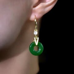 Gold green jade donut dangle earring worn on ear against dark background