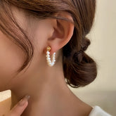 Close-up of woman wearing dainty freshwater pearl hoop earring with gold ball stud