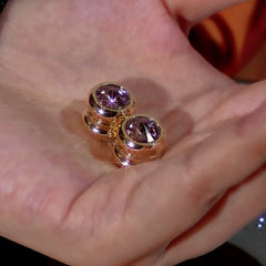 Pair of sparkly gold bezel set round purple gem stud earrings resting on a palm