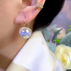 Gold iridescent blue glass drop earring worn on ear with crystal ear cuff
