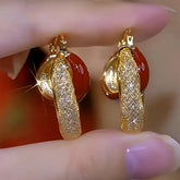 Pair of gold textured pave red gem hoop earrings held between fingers