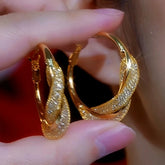 Pair of sparkling twisted gold hoop earrings held between fingers
