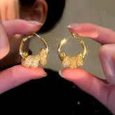 Pair of gold glittery cluster drop hoop earrings held between fingers, close-up