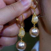 Hand holding pair of gold pave teardrop pearl drop huggie hoop earrings