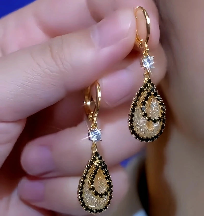 Pair of gold teardrop dangle earrings with black trim and clear crystal held in hand