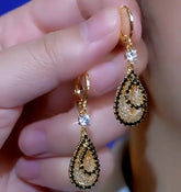 Pair of gold teardrop dangle earrings with black trim and clear crystal held in hand