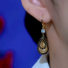Gold black-trimmed teardrop crystal dangle earring worn on a person's ear