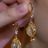 Closeup of hand holding gold teardrop crystal dangle hoop earrings