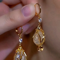 Closeup of hand holding gold teardrop crystal dangle hoop earrings