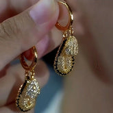 Hand holding pair of gold two-tier textured teardrop hoop dangle earrings with black trim