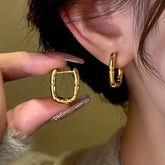 Gold square bamboo hoop earring held beside ear with matching earring worn