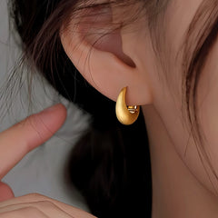 Matte gold chunky teardrop huggie hoop earring worn on a woman's ear