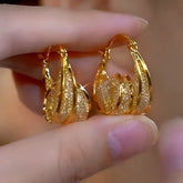 Pair of layered twisted textured gold teardrop hoop earrings held in hand