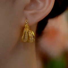 Textured gold teardrop hoop earring worn on ear, alternate side view