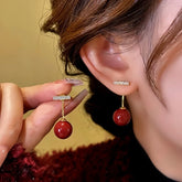 Gold crystal bar red bead drop dangle earrings, one held in hand, one worn on ear