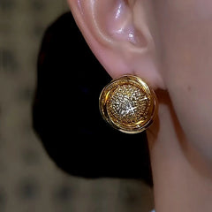 Gold round pave crystal stud earring worn on a person's ear, close-up