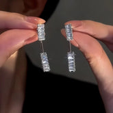 Pair of sparkling silver rectangular crystal drop earrings held between fingers