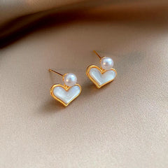 Pair of gold mother of pearl heart stud earrings with pearl accent on beige satin fabric