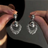 Pair of silver rhinestone crescent dangle earrings held by hands