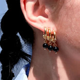 Gold triple huggie hoop illusion earring with black bead drops worn on ear