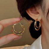 Gold double hoop earring with clasp, held next to a worn matching earring