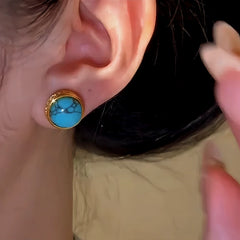 Side angle close-up of gold turquoise stud earring worn on a person's earlobe