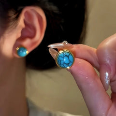 Gold bezel veined turquoise stud earring held by hand, matching worn earring in background