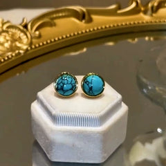 Gold bezel round veined turquoise stud earrings on white velvet jewelry display