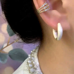 White enamel huggie hoop earring and layered crystal ear cuff on right ear