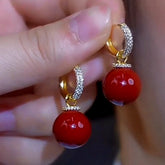 Pair of glossy red bead drop hoop earrings with crystal pave detail, held in hand