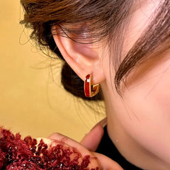 Side angle view of red enamel gold small hoop earring worn on ear