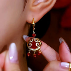 Chinese-style red ruyi lock dangle earring, closeup of gold drop earring worn on ear
