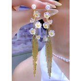 Pair of iridescent white flower gold tassel pearl stud long drop earrings held in hand