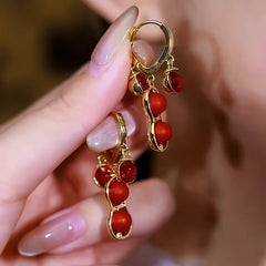 Pair of gold red peanut bead dangle hoop earrings held by manicured hand