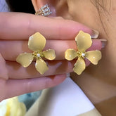 Women's yellow enamel flower pearl stud earrings held between fingers
