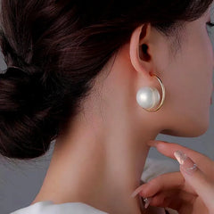 Large white pearl gold open hoop earrings on woman, side profile with dark low bun