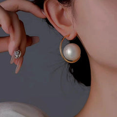 Elegant gold open hoop earring with large white pearl, worn on woman's ear