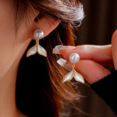 Gold pearl mermaid tail drop earrings: one worn on ear, one held to show detail