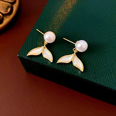 Pair of gold pearl mermaid tail drop earrings on dark green jewelry box