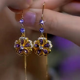 Pair of gold purple crystal flower drop earrings held in hand closeup