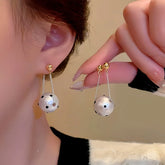 White polka dot pearl ball drop earrings with gold stud, worn on ear and held in hand